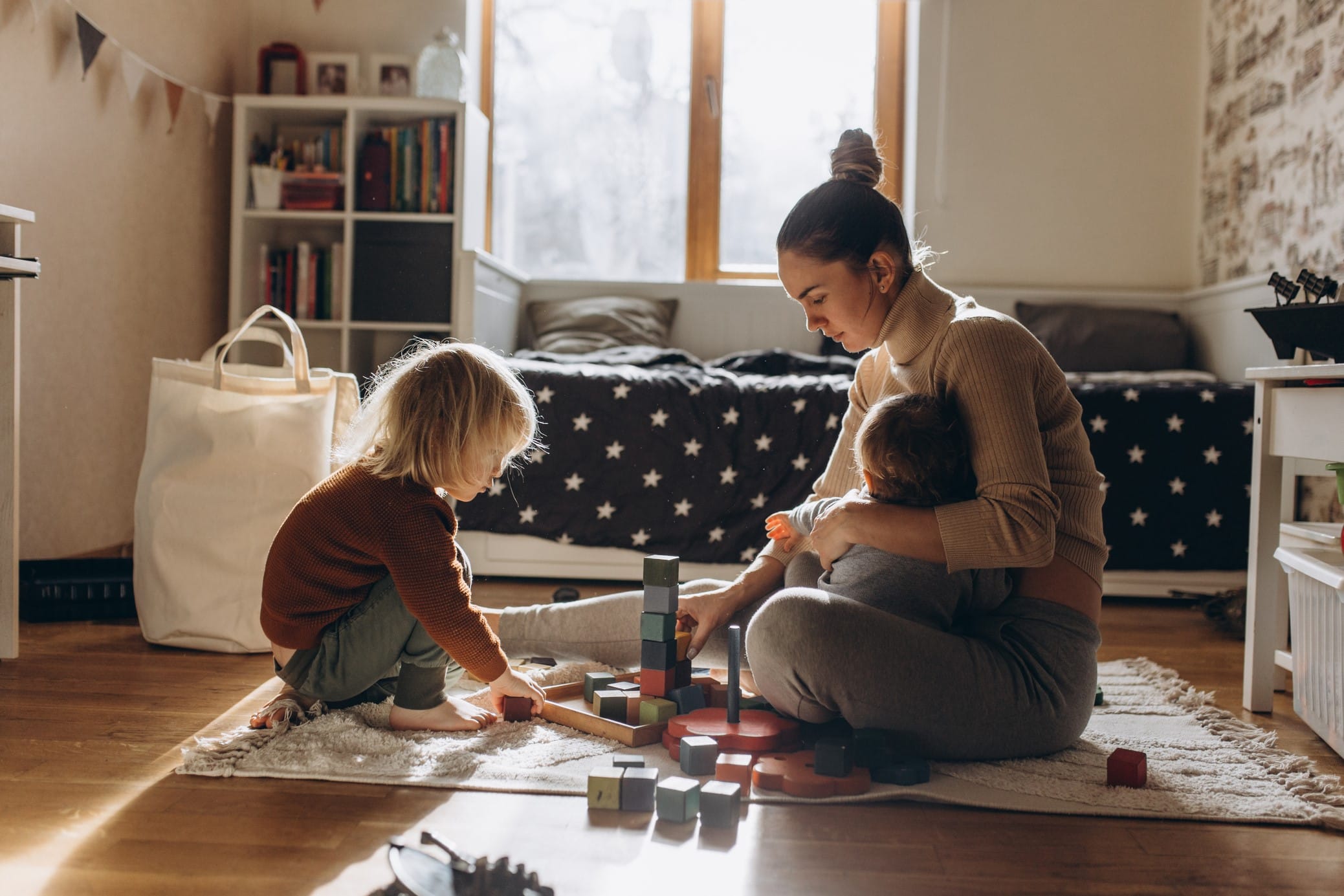 Mother playing with young child while holding baby