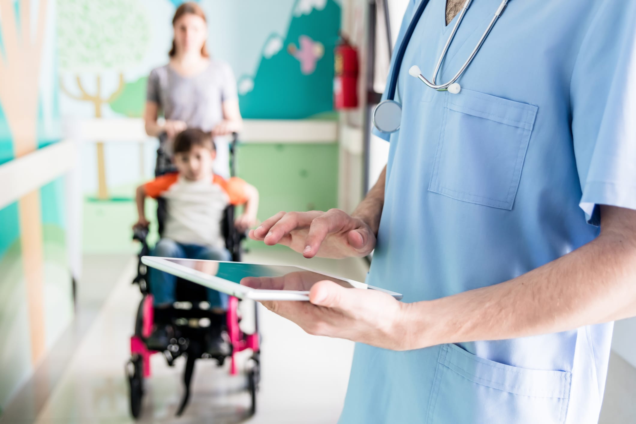 Close up of unrecognizable doctor checking the medical chart of his patient on wheelchair and mom standing behind her son