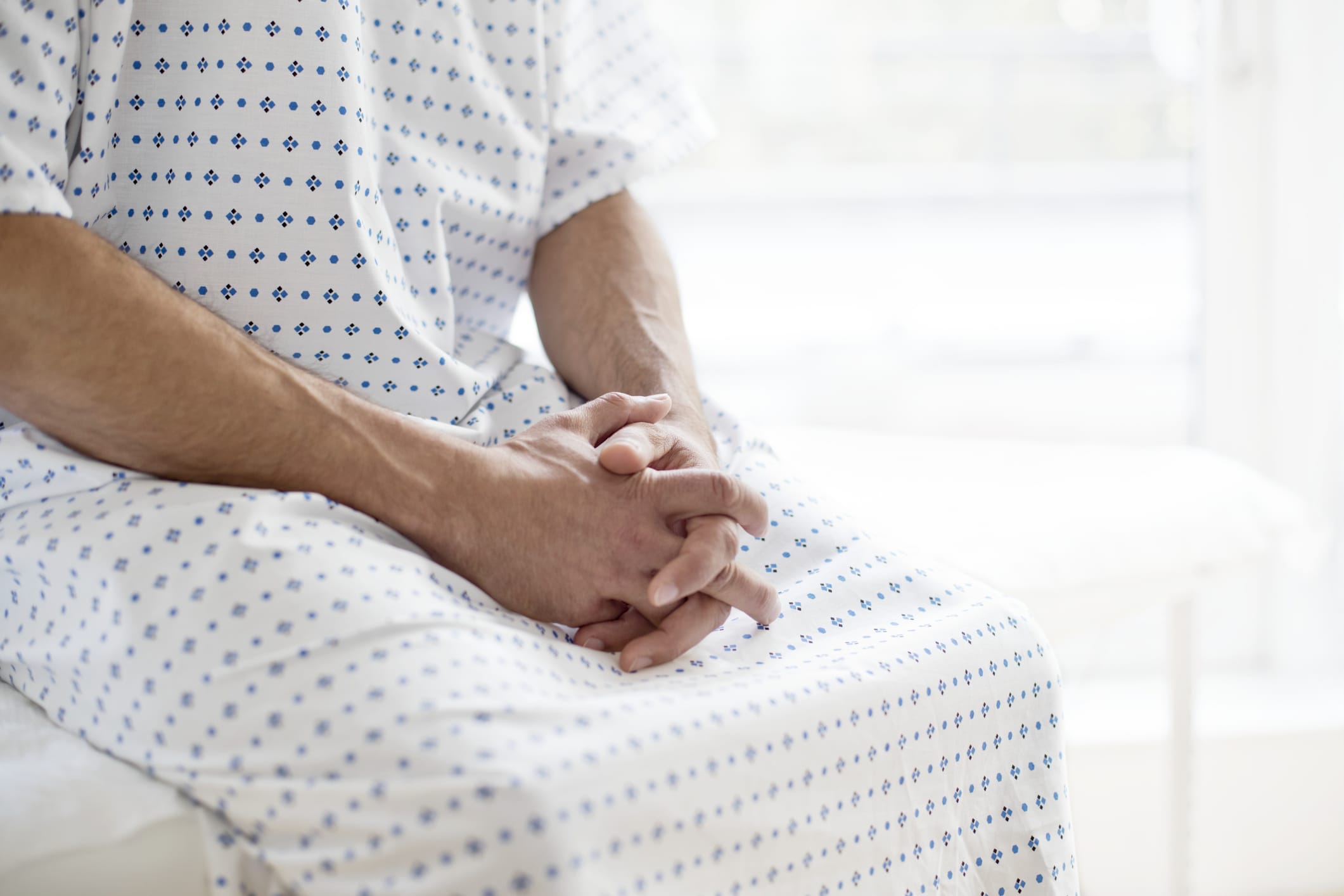 Male patient wearing hospital gown sitting on bed.
